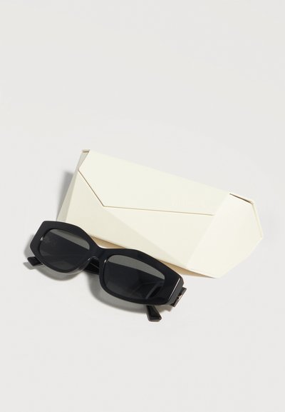 Μαύρα ορθογώνια γυαλιά ηλίου δίπλα σε μια κλειστή, κρεμ χρωματιστή γεωμετρική θήκη γυαλιών σε μια απλή φωτεινή επιφάνεια.