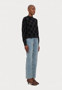 Sweater court à carreaux noirs avec une texture métallique, associé à un jean droit bleu clair et des sandales à talons noires à lanières.