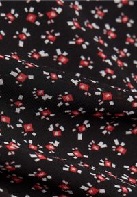 Tessuto nero con un motivo geometrico ripetuto in rosso, bianco e rosa, caratterizzato da una consistenza liscia e una leggera lucentezza.
