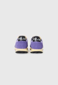 Purple suede sneakers with a beige sole. Black “VEJA” logo on heel, minimalistic design, textured material, rubber outsole for grip.