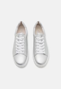 Paire de baskets basses métalliques argentées avec lacets blancs et semelles épaisses blanches en caoutchouc, vues de dessus sur un fond uni.