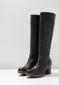 Knee-high black leather boots with a rounded toe, block heel, and stitched detailing along the sole. Smooth texture and minimal accents.