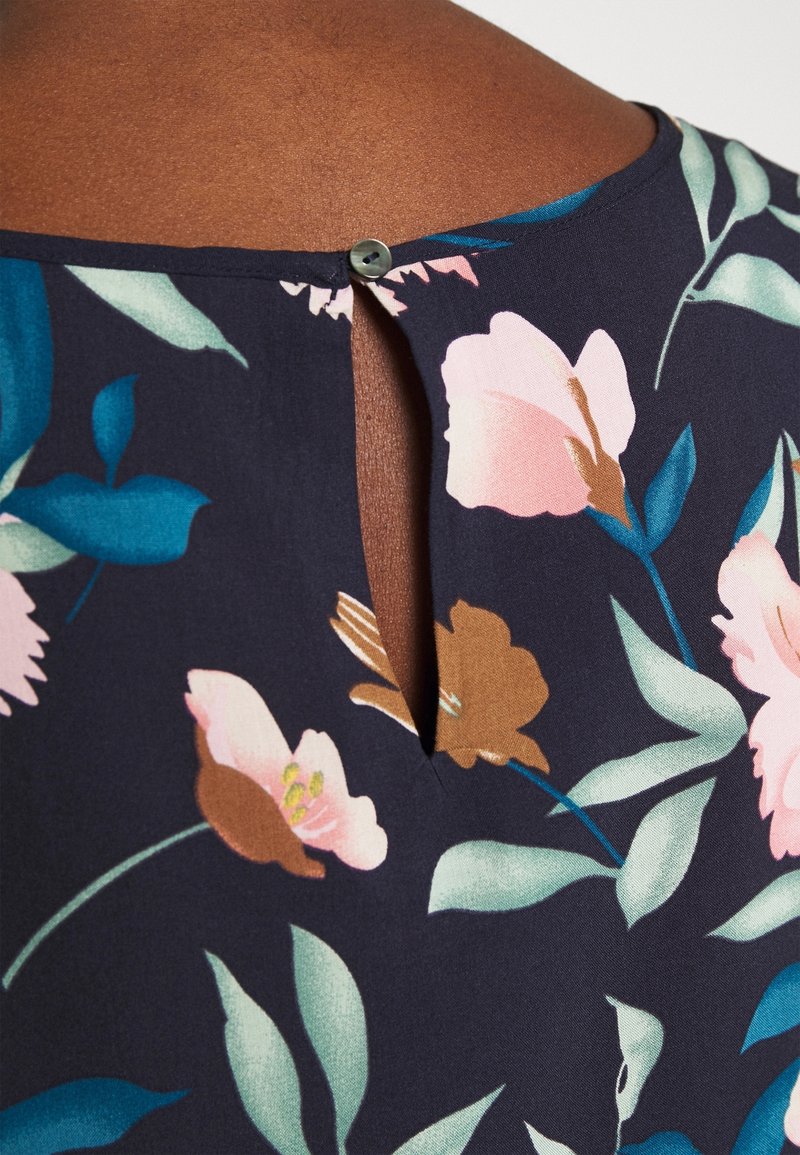 Haut à imprimé floral avec un fond bleu marine, orné de fleurs roses et brunes. Comprend une petite ouverture en forme de goutte à l'arrière avec un bouton.