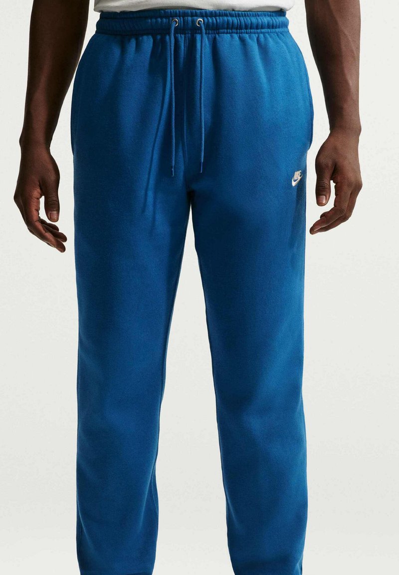 Blåa sweatpants med dragsko i midjan, sidofickor och en liten vit Nike-logotyp på vänster sida. Tillverkade av mjukt tyg.