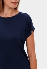 Námorně modrá krátká rukávová košile s kulatým výstřihem. Měkká, hladká tkanina s volným střihem. Jemná textura na povrchu.