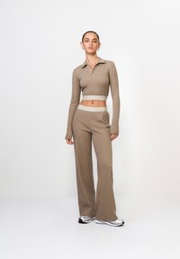Beżowy, prążkowany dwuczęściowy zestaw składający się z krótkiej długosleeveowej koszulki polo z kołnierzykiem oraz spodni z wysokim stanem i szerokimi nogawkami z elastycznym pasem.