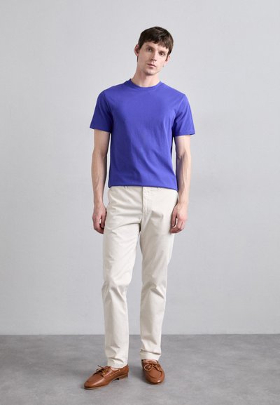 Blue cotton t-shirt with short sleeves, paired with beige chinos and brown boat shoes. The look is casual and fitted.
