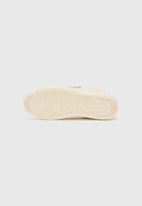 Shoe sole in light beige rubber, featuring a textured surface with circular patterns and a smooth rounded toe area. Minimal branding visible.