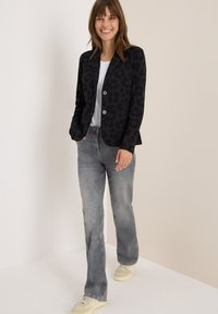 Zwarte blazer met een subtiele luipaardprint, twee knopen en zijzakken, gecombineerd met grijze rechte spijkerbroeken en sneakers.