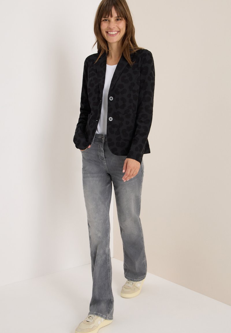 Zwarte blazer met een subtiele luipaardprint, twee knopen en zijzakken, gecombineerd met grijze rechte spijkerbroeken en sneakers.
