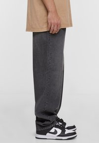 Vaqueros de mezclilla gris con un ajuste holgado, combinados con zapatillas en blanco y negro que tienen un logo de swoosh prominente.