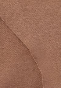 Tissu textile dans une teinte marron chaud avec une texture côtelée, montrant des sections superposées et des détails de couture fins.