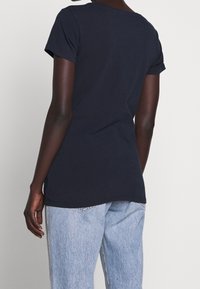 Navyblauwe katoenen T-shirt met korte mouwen, ronde hals en een licht gebogen zoom, gecombineerd met lichtblauwe jeans met zijstrepen.