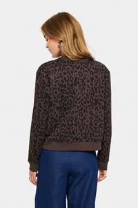 Sweatshirt marron avec imprimé léopard noir, poignets et ourlet côtelés. Présente une coupe décontractée et un col rond. Associé à un pantalon large bleu.