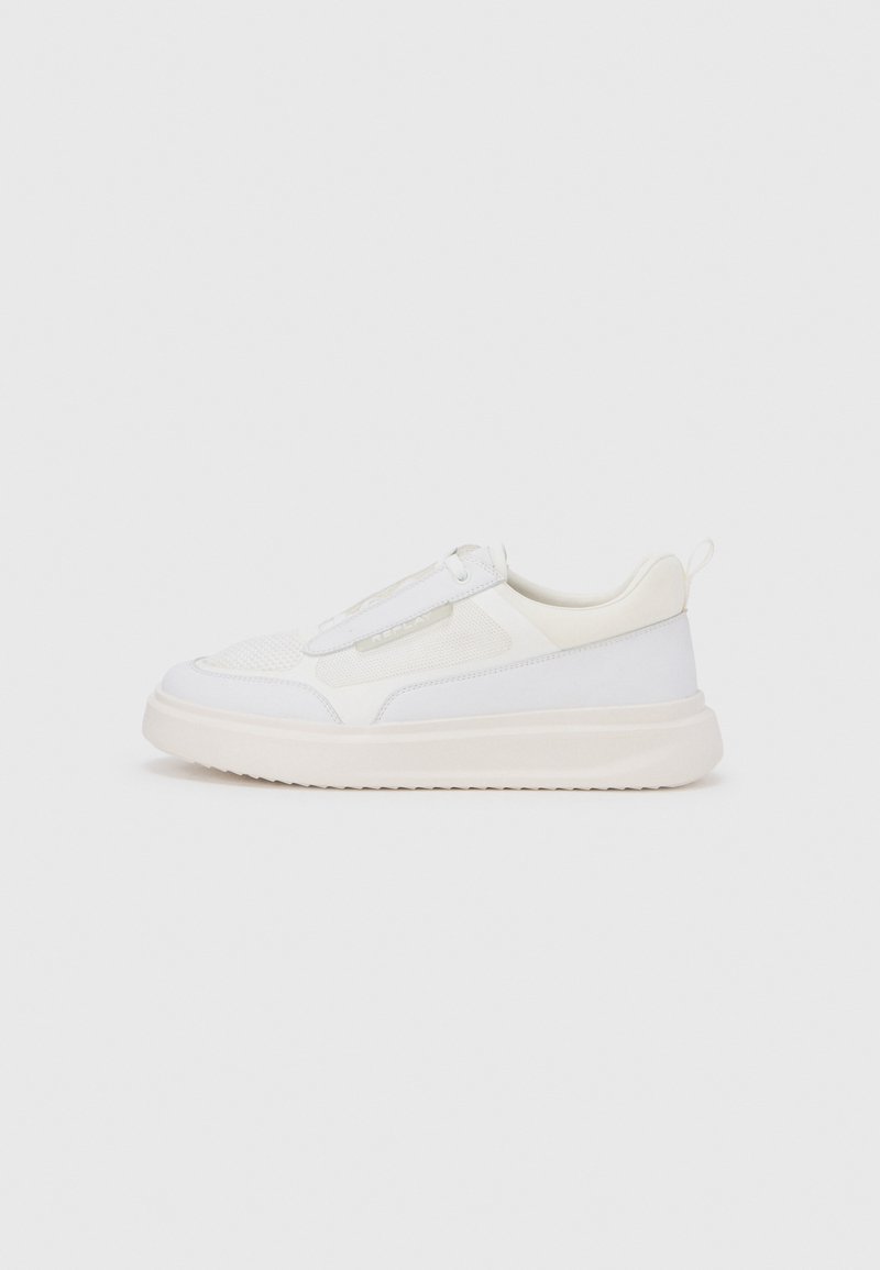 Λευκά αθλητικά παπούτσια με υφασμένη ανάγλυφη επιφάνεια από δίχτυ, λείες δερμάτινες λεπτομέρειες και χοντρή καουτσούκ σόλα. Διαθέτουν θηλιά για εύκολο φόρεμα.