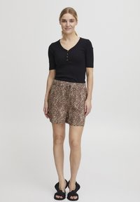 Čierny rebrovaný top s krátkym rukávom a detailom gombíkov, spolu s hnedými šortkami s leopardím vzorom. Model nosí čierne uzlové šľapky.