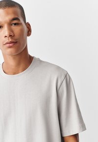 Vaaleanharmaa puuvillainen T-paita, jossa on pyöreä pääntie ja lyhyet hihat. Päällä on sileä pinta ja rento istuvuus. Ei näkyviä kuvioita tai yksityiskohtia.