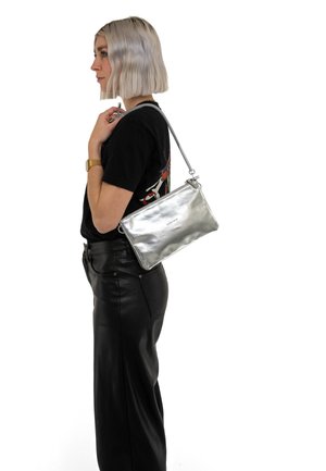 Borsa a spalla in pelle argentata con una trama liscia, forma rettangolare e chiusura con zip. Indossata in modo casual con un outfit nero.