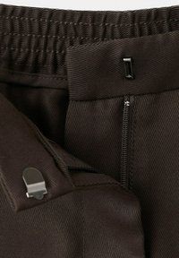 Pas pas z elastičnim trakom, kovinsko zaponko z zatičem in delno videnim zadrgo na teksturirani tkanini, temno rjave barve.