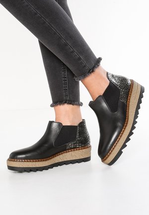 Sorte ankelstøvler med kilehæl, textured hældetalje og takkede såler, båret med sorte skinny jeans med frynset kant.