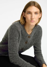 Cardigan grigio in lana con finitura testurizzata, caratterizzato da grandi bottoni marroni, scollo rotondo e maniche lunghe.