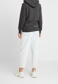 Kohlgrauer Kapuzenpullover aus weichem Stoff mit gerippten Bündchen, kombiniert mit hellblauen, locker sitzenden Jeans und weißen Turnschuhen, von hinten gesehen.