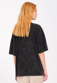 Camiseta negra de gran tamaño con textura de lavado mineral, que presenta mangas cortas y un escote redondo, con un corte relajado y diseño de hombros caídos.