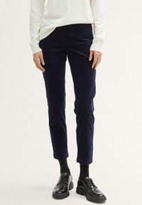 Mörkblå kordflossbyxor med avsmalnad ben, som har en knappstängning, bälteshällor och subtil textur, tillsammans med svarta läderskor.