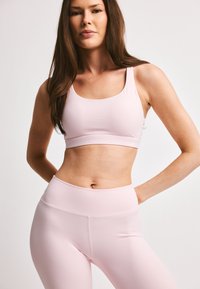 Lys rosa sports-BH og høyt midje tights laget av et glatt, elastisk stoff, med et minimalistisk design og uten synlige mønstre.