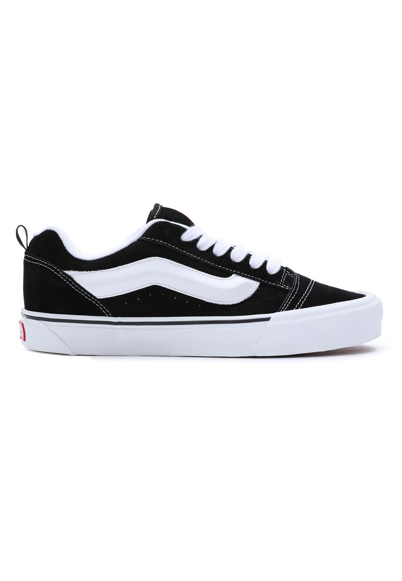 Black suede sneakers with white accents, featuring a low-top design, lace-up closure, and a thick white rubber sole. Brand logo on heel.