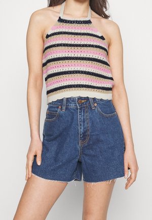 Kobieta ubrana w niebieskie, dżinsowe szorty z wysokim stanem oraz bezrękawnik halter z poziomymi paskami w kolorach różowym, beżowym, czarnym i kremowym.