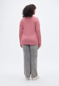 Κόκκινη και λευκή ριγέ μπλούζα με μακριά μανίκια σε συνδυασμό με γκρι παντελόνι φαρδύ στο κάτω μέρος. Η μπλούζα έχει στρογγυλή λαιμόκοψη και εφαρμοστή γραμμή με ομαλή υφή υφάσματος.