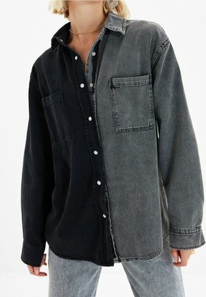 Spijkerblouse met een gesplitst ontwerp; de ene kant zwart, de andere donkergrijs. Voorzijde met knopen en een enkele borstzak. Zachte textuur.
