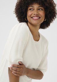 Maglione strutturato di colore crema con maniche corte e puffate e scollatura arrotondata. Il tessuto a maglia liscia accentua la sua morbidezza complessiva.
