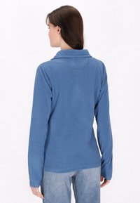 Maglione in pile azzurro chiaro con maniche lunghe e colletto ripiegato. Texture morbida, design semplice e orlo leggermente curvo in vita.