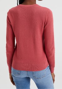Pletený svetr v korálové barvě, texturovaná látka, s žebrovanými manžetami a lemem. Má kulatý výstřih a volný střih.