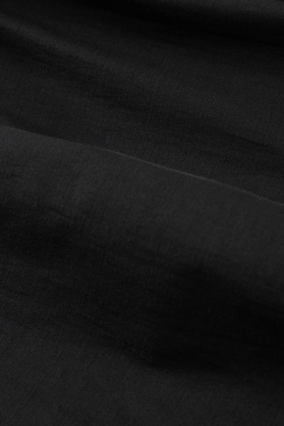 Gros plan sur un tissu noir avec une texture visible et des plis doux créant des variations d’ombre.