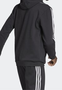 Zwarte hoodie met witte zijstrepen, voorzien van een relaxte pasvorm, ribgebreide manchetten en zoom, gemaakt van zachte stof.