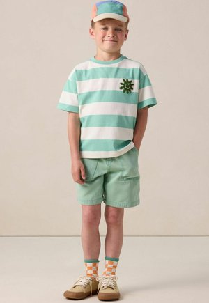 Chemise à rayures vert menthe à manches courtes avec broderie de soleil, associée à un short assorti, une casquette multicolore et des chaussettes à carreaux avec des chaussures beiges.