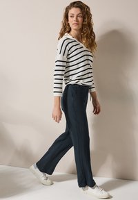 Maglione a righe in bianco e blu navy; vestibilità rilassata. Pantaloni a strappo blu navy scuro con tasche laterali. Sneakers bianche.