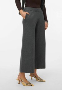 Pantalon gris à jambes larges en tissu doux avec une ceinture côtelée et des poches latérales, associé à des chaussures à lanières jaunes ornées d'un imprimé serpent.