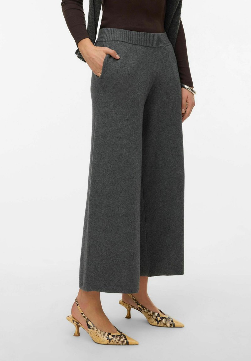 Pantalon gris à jambes larges en tissu doux avec une ceinture côtelée et des poches latérales, associé à des chaussures à lanières jaunes ornées d'un imprimé serpent.