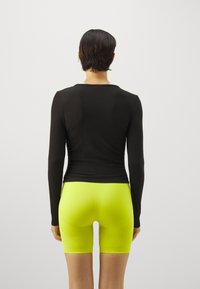 Top nero a maniche lunghe con una vestibilità aderente e texture a costine, abbinato a pantaloni corti neon verde brillante, che mostrano una finitura liscia.