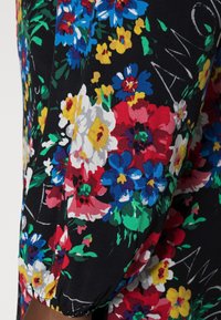 Mouw van zwarte stof met een kleurrijk bloemenpatroon met rode, blauwe, gele, witte bloemen, groene bladeren en subtiele witte tekstdetails.