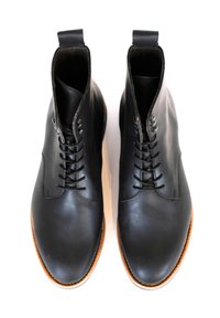 Stivali ankle in pelle nera con texture liscia, punta rotonda e lacci sottili. Presentano una suola in gomma marrone chiaro e una linguetta sul tacco.