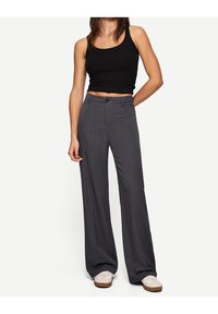 Grijze wijde broek gemaakt van een gestructureerde stof, met een knoopsluiting aan de voorkant en zijzakken, gecombineerd met een zwart tanktop.