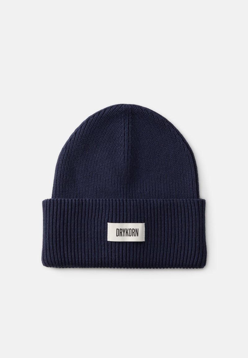 Námořnická modrá pletená čepice s ohrnutým lemem. Má ribbovaný povrch a malou obdélníkovou etiketu s nápisem „DRYKORN“ černým písmem.