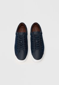 Baskets en daim navy avec des accents en cuir, semelles en caoutchouc blanc et lacets plats. Présente un logo sur la languette et une finition lisse et mate.