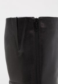 Botín de cuero negro hasta la rodilla, con corte recto, cremallera YKK a lo largo del costado y una textura suave con un brillo sutil.