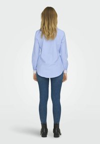 Lichtblauw gestreefd shirt met lange mouwen, afgeronde zoom, gecombineerd met donkerdenim leggings en zwarte enkellaarsjes.
